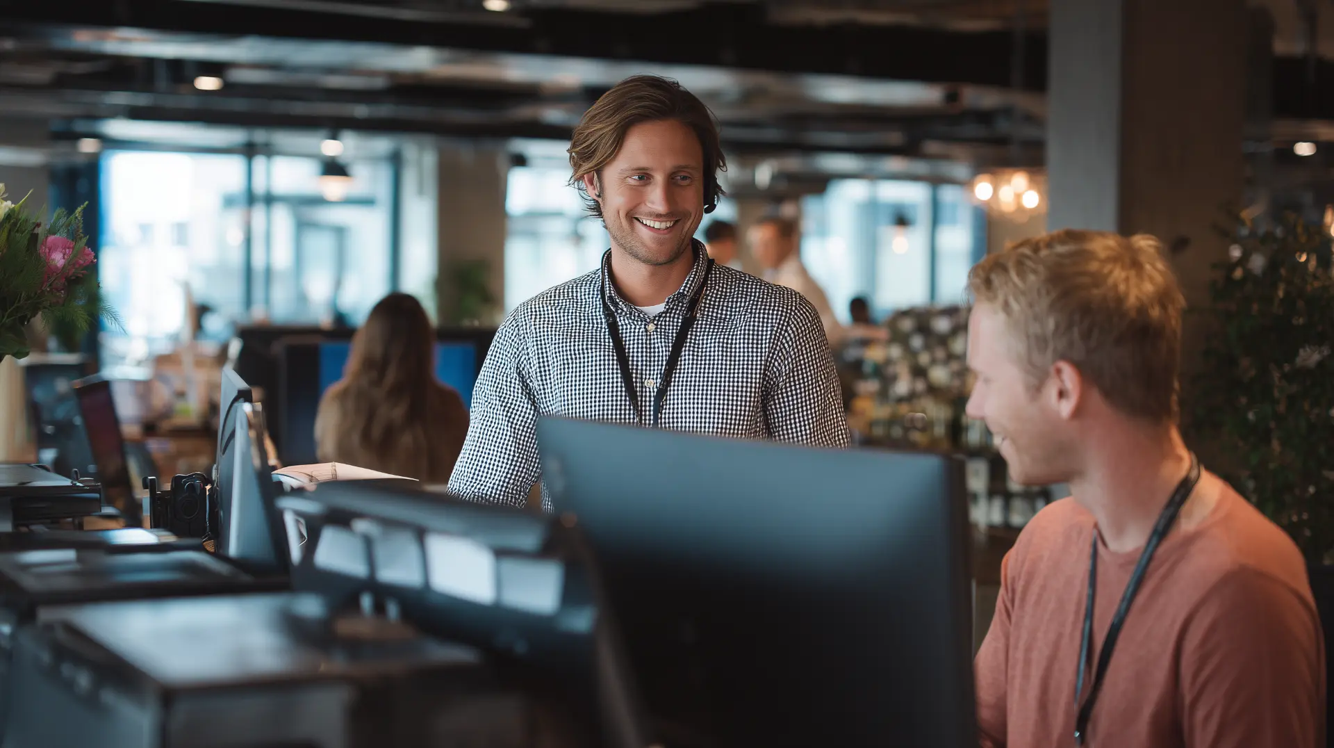 Friendly IT support technician helping a colleague at a modern office workstation