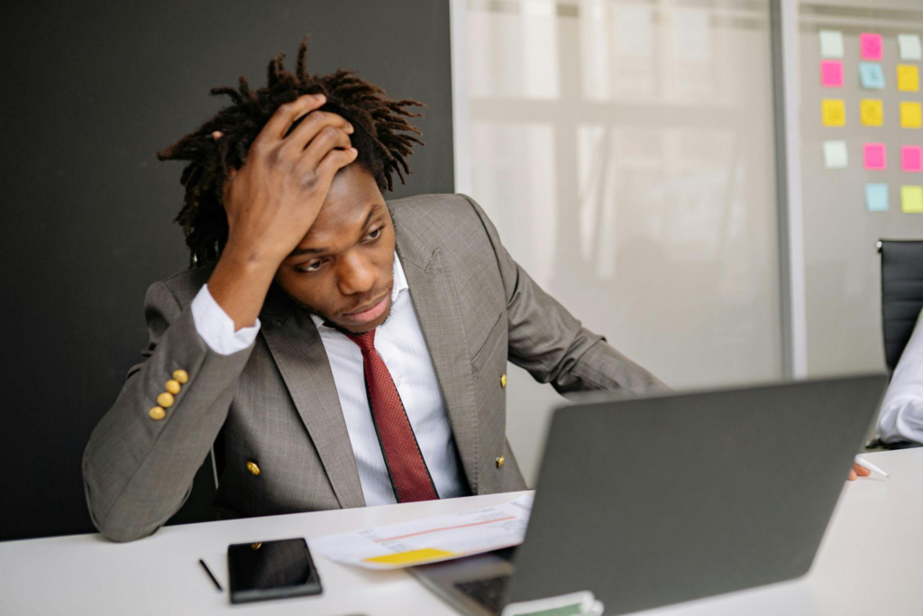 A stressed businessman holding his head while looking at a laptop.