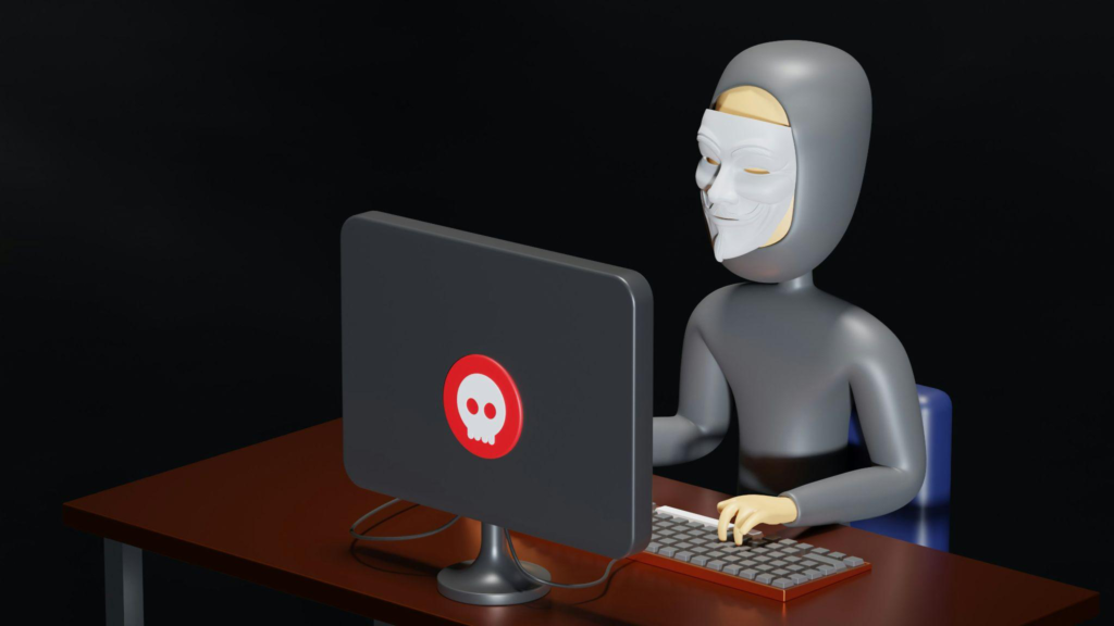 A masked hacker sitting at a desk using a computer screen with a red warning symbol.