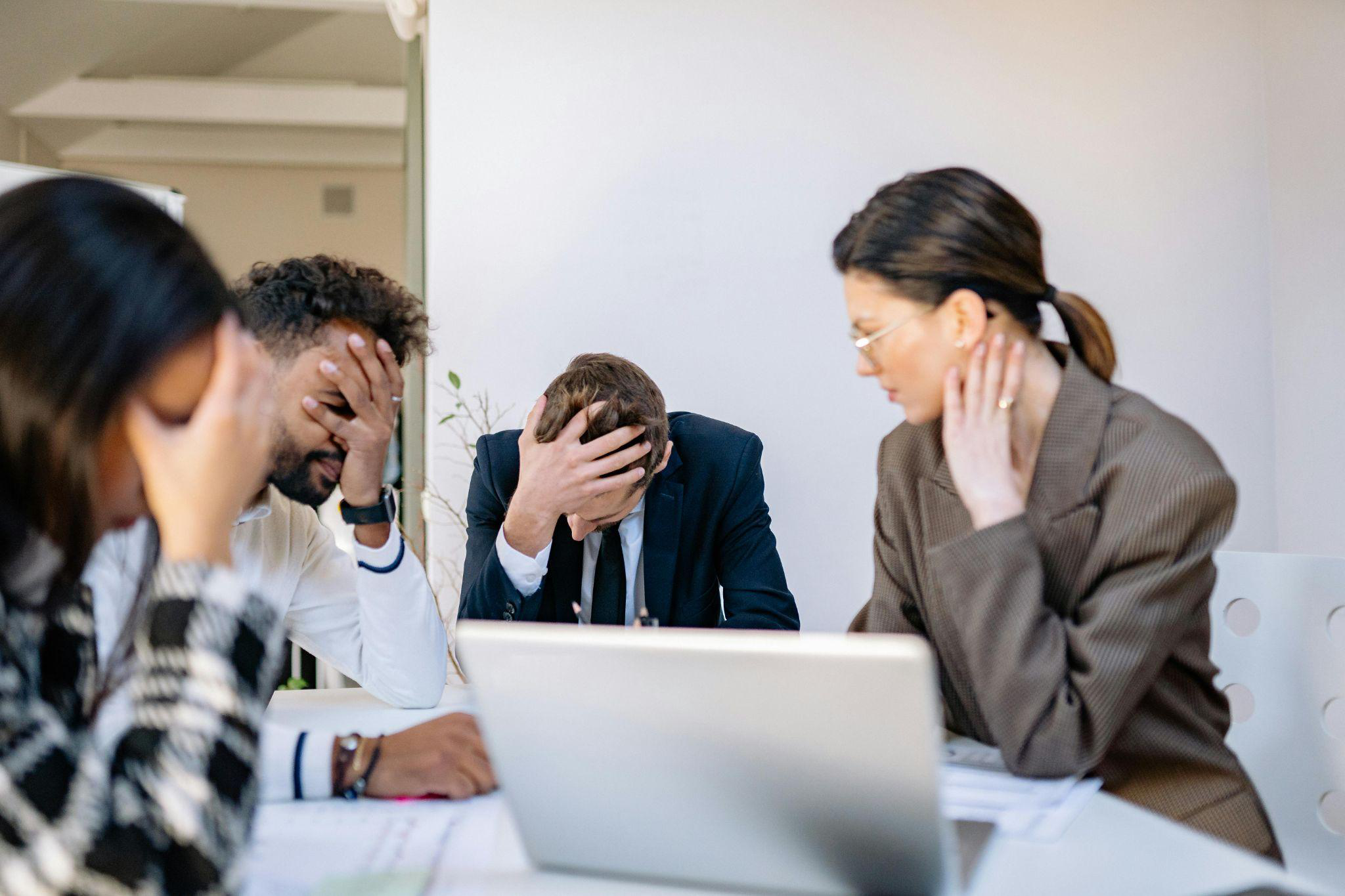 A group of business professionals sitting at a desk, looking stressed.