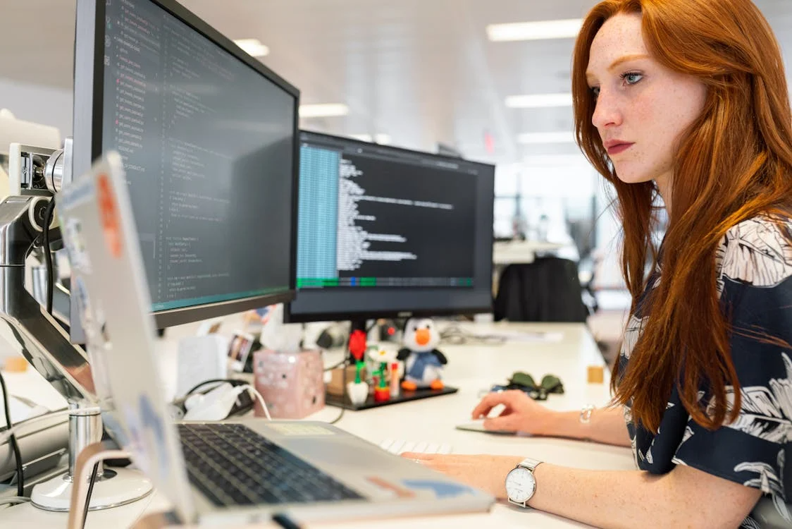 An image of a woman working on a laptop and computer screen.